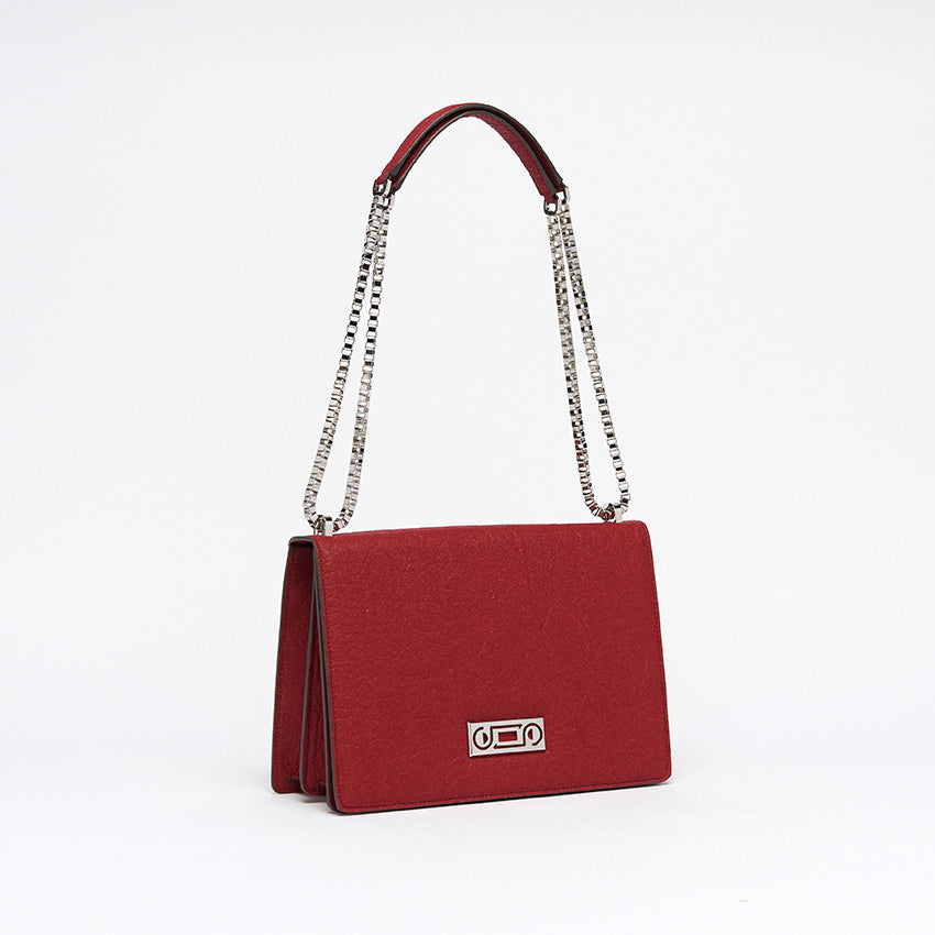 The Cristiana Vegan Shoulder Bag by Studio Tondini. Three-quarter view of the cherry red version, highlighting the radiant chain plated in real palladium and the sculptural structure crafted from Piñatex®.